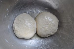 two pizza dough balls proofing in a bowl