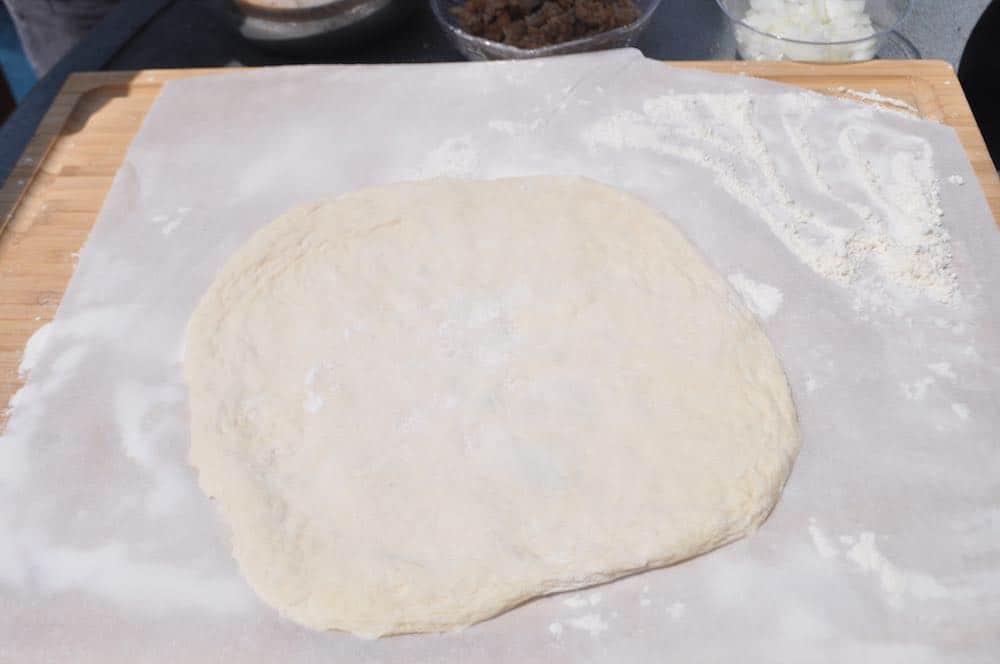 a spread out pizza dough on parchment paper to make a smoked pizza