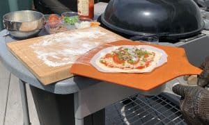 putting a pizza on a pizza peel to put in the grill or smoker