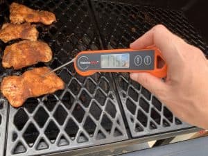 a instant thermometer showing 175 degree internal temperature of smoked boneless chicken thighs