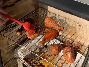 basting sauce on smoked chicken legs in a masterbuilt electric smoker