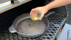 about to pour melted butter in cast iron skillet on pellet grill smoker