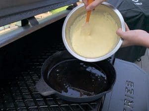 pouring smoked cornbread batter into preheated cast iron skillet