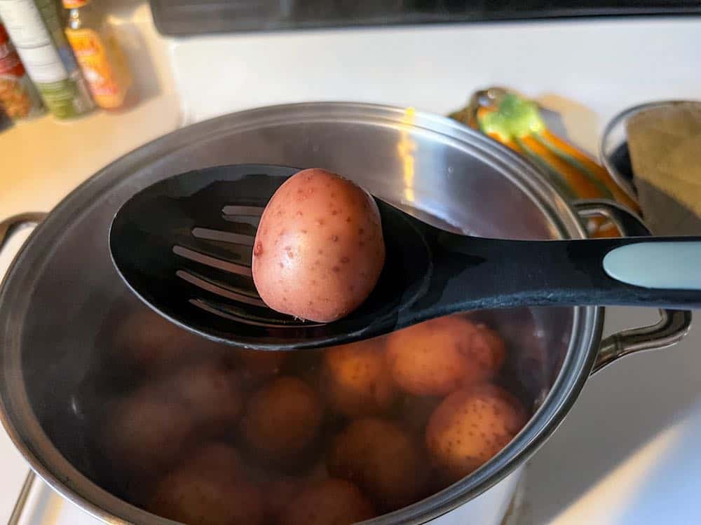 taking a boiled red potato out of a pot with a slotted spoon