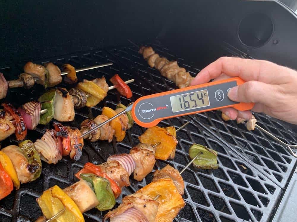 checking the internal temperature of the smoked chicken kabob skewers with an instant read thermometer reading 165°F