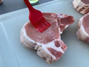 brushing oil on a raw pork chop