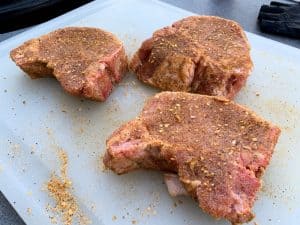 seasoned raw pork chops on a cutting board