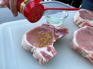 sprinkling seasoning on a raw pork chop