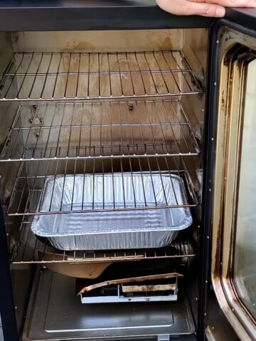 A Masterbuilt electric smoker open to reveal the cooking racks and an empty aluminum foil pan on the bottom rack