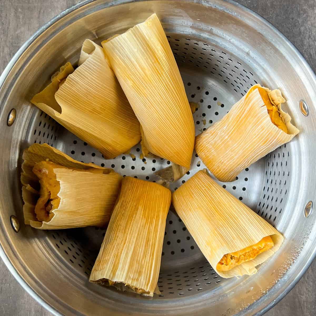 tamales steaming in a steamer basket insert of a pot