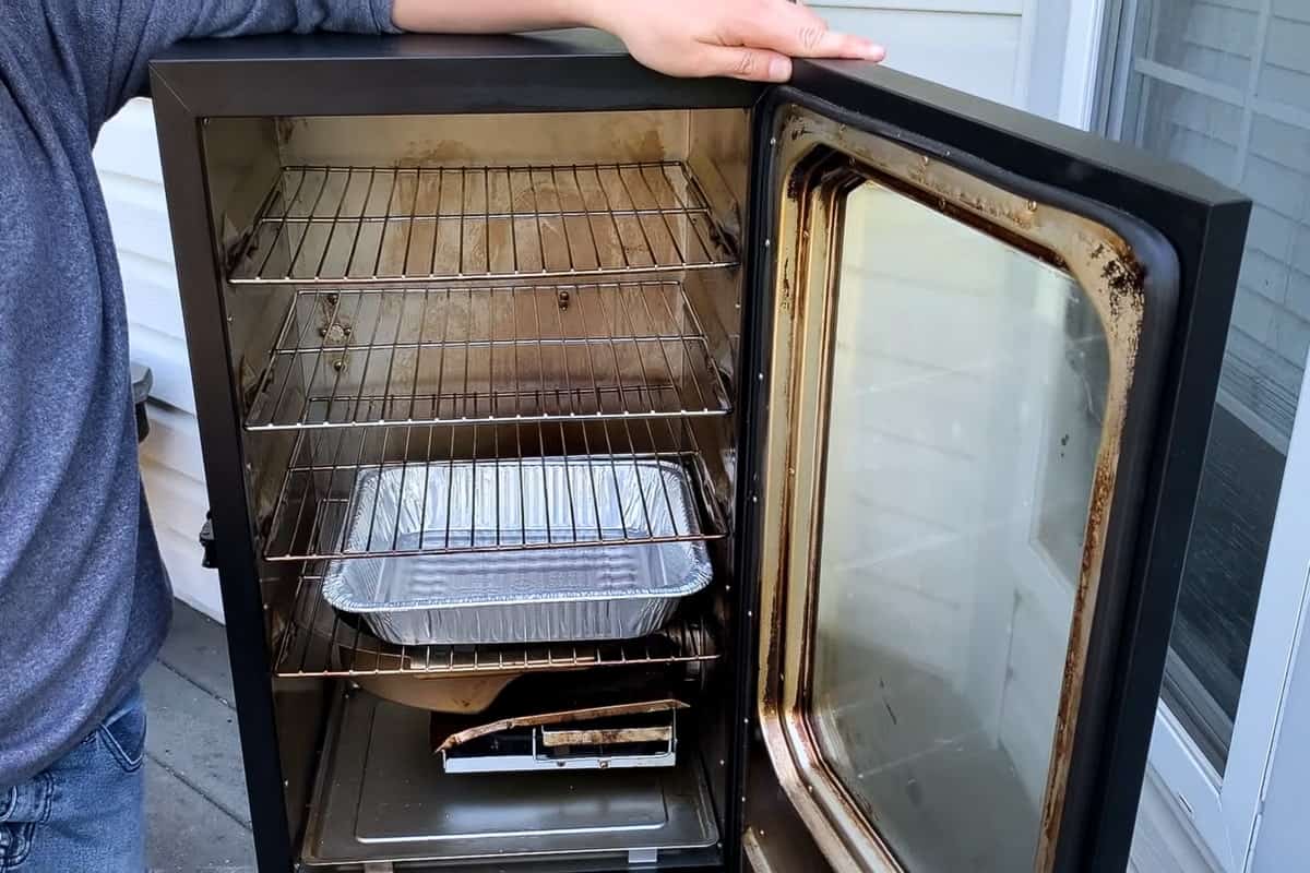 A Masterbuilt electric smoker open to reveal the cooking racks and an empty aluminum foil pan on the bottom rack