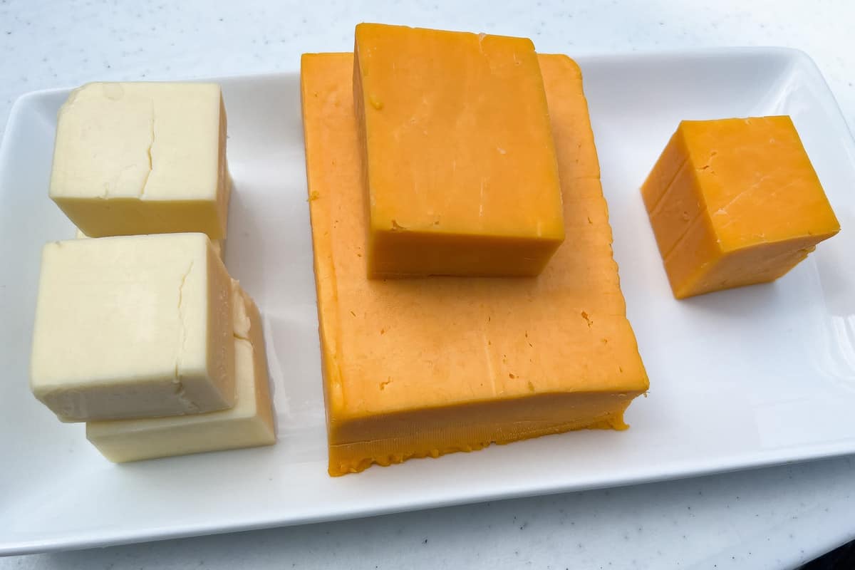 gruyere and cheddar blocks of cheese on a white platter
