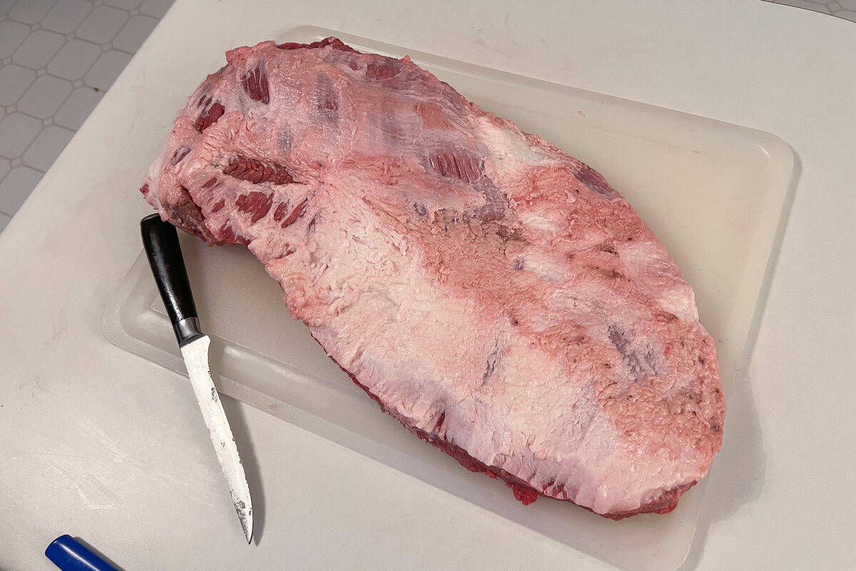 a full packer beef brisket fat cap side up on a white cutting board with a knife next to it