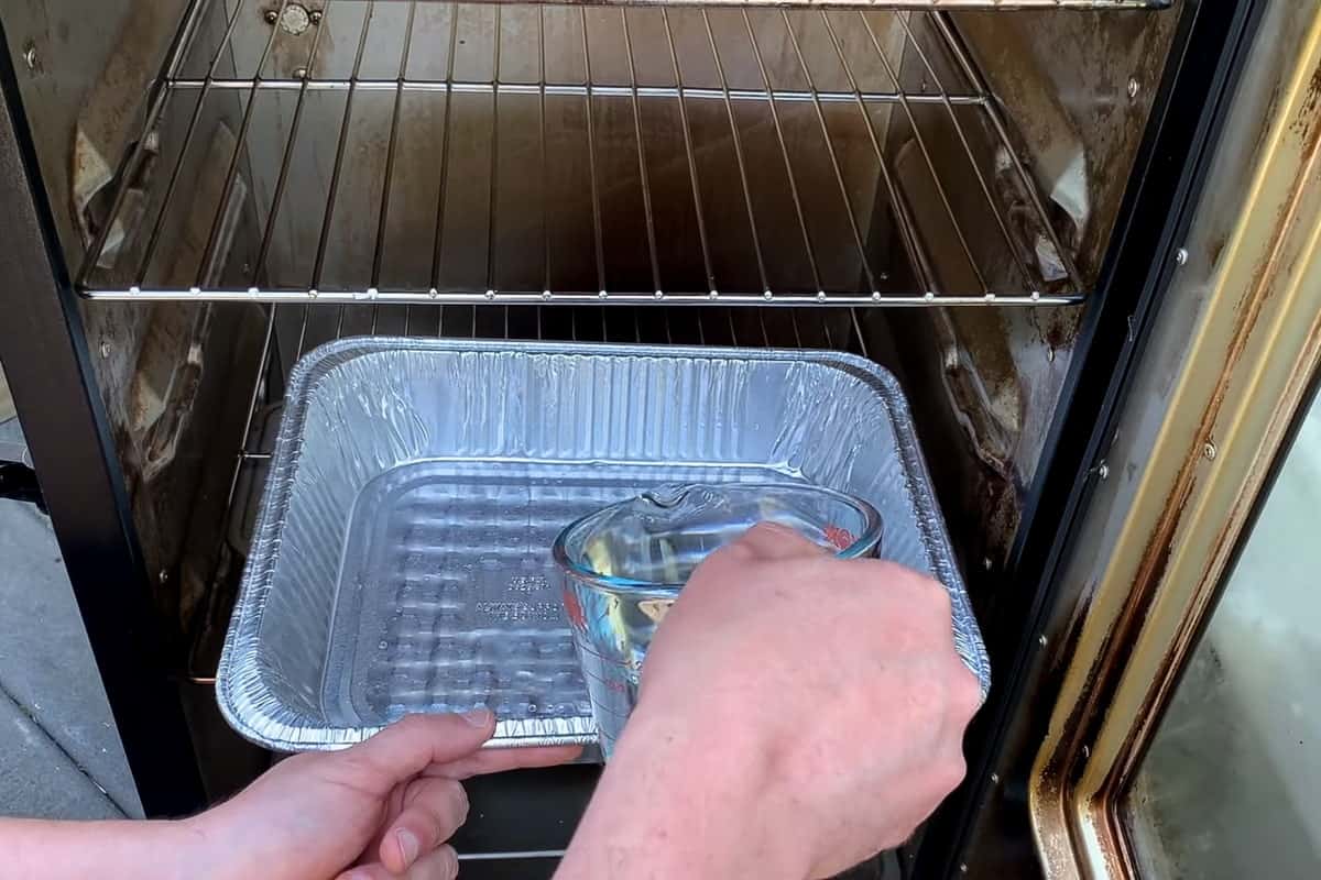 pouring water in the aluminum foil pan on the bottom shelf of a masterbuilt electric smoker