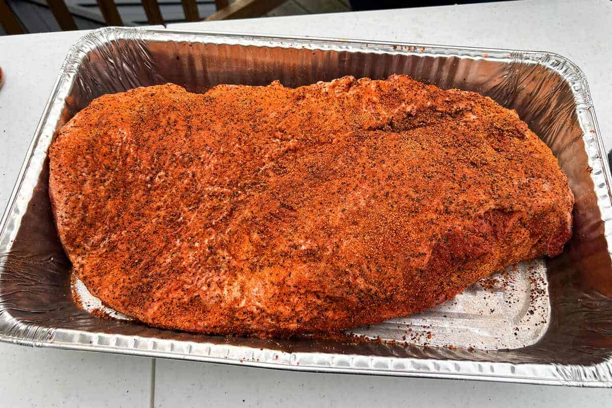 a raw seasoned beef brisket in an aluminum foil pan