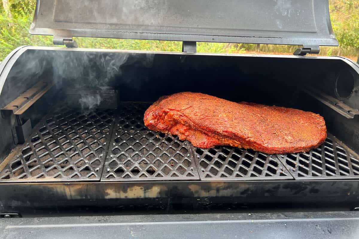 a brisket on the grates of the Pit Boss with the larger side to the left and a firebox smoking in the back left of the grill