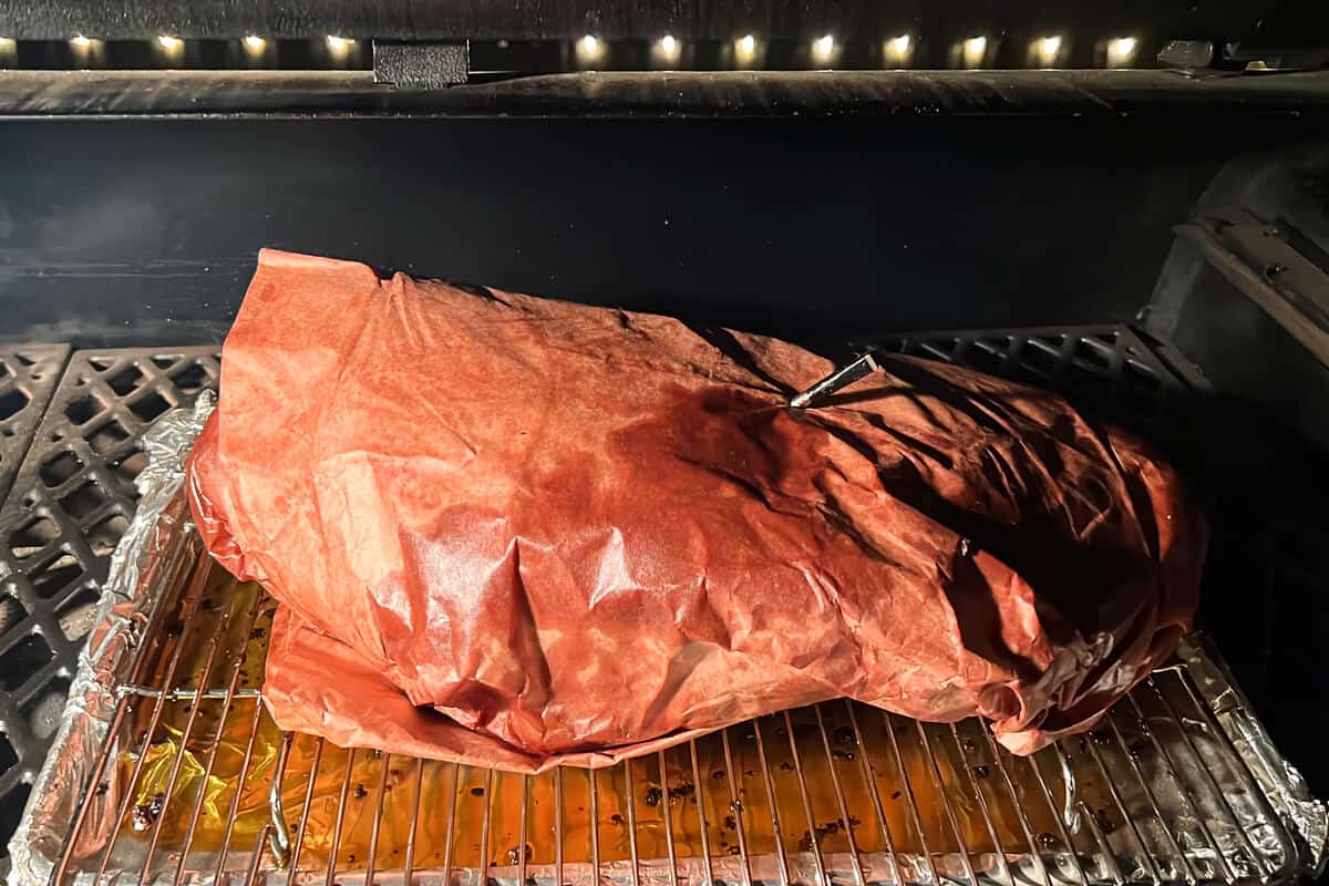 a brisket wrapped in butcher paper on a wire rack in a pit boss with a MEATER thermometer probe inserted into the meat through the butcher paper