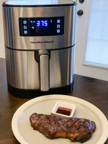 an air fryer on a table next to a plate with a steak on it