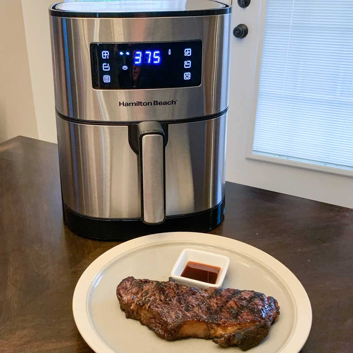 an air fryer on a table next to a plate with a steak on it