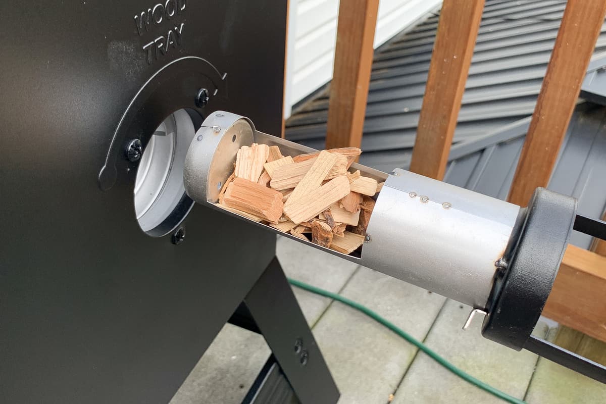 Wood chips being fed into the wood tray of a masterbuilt electric smoker