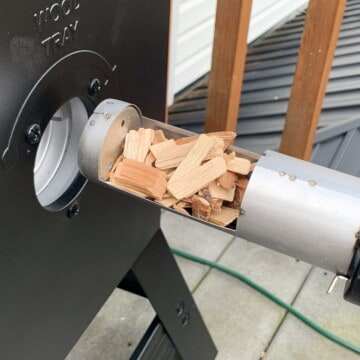 Wood chips being fed into the wood tray of a masterbuilt electric smoker