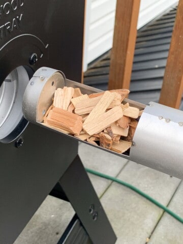 Wood chips being fed into the wood tray of a masterbuilt electric smoker