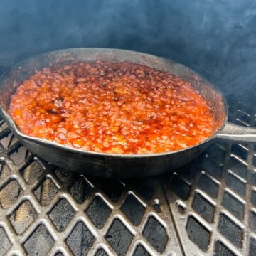 pit boss smoked baked beans in a cast iron pan on the grill grates