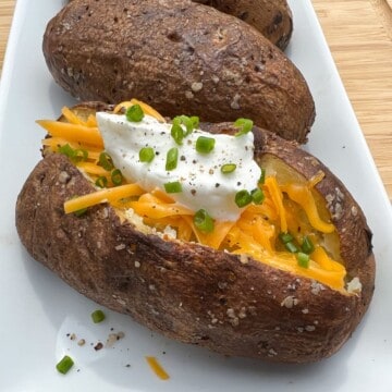 Smoked baked potatoes with cheese, sour cream and chives on a white plate