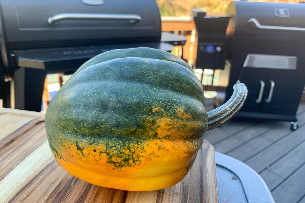 an acorn squash on a cutting board in front of some pellet grills