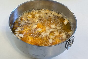 a bowl of water with pumpkin seeds and pulp floating in it