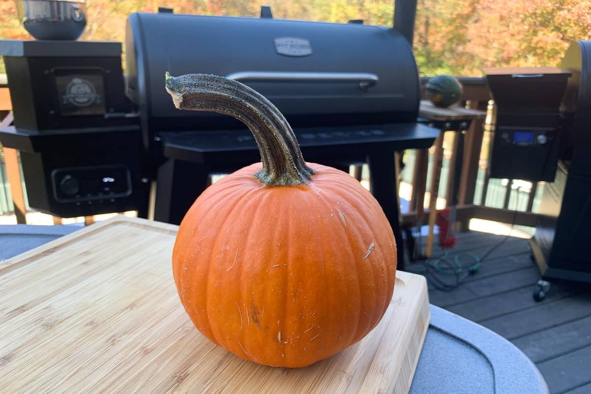 a pie pumpkin on a cutting board in front of smokers