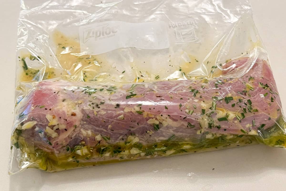 a raw pork tenderloin in a gallon sized bag filled with garlic herb marinade