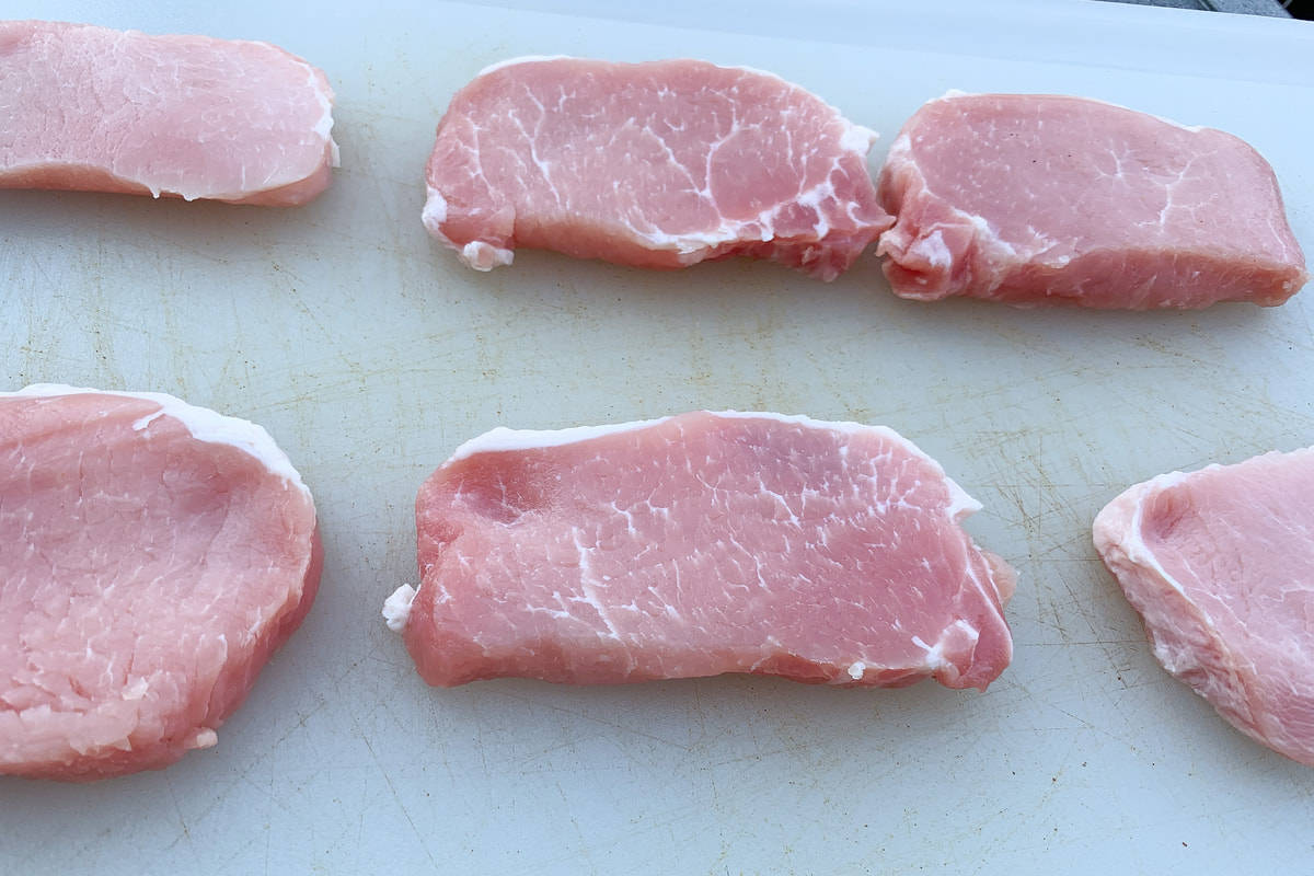 raw boneless pork chops on a white cutting board