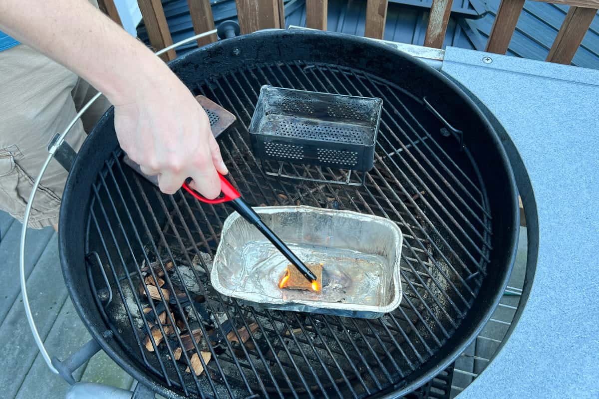 lighting a firestarter cube inside an aluminum foil loaf pan on a charcoal grill