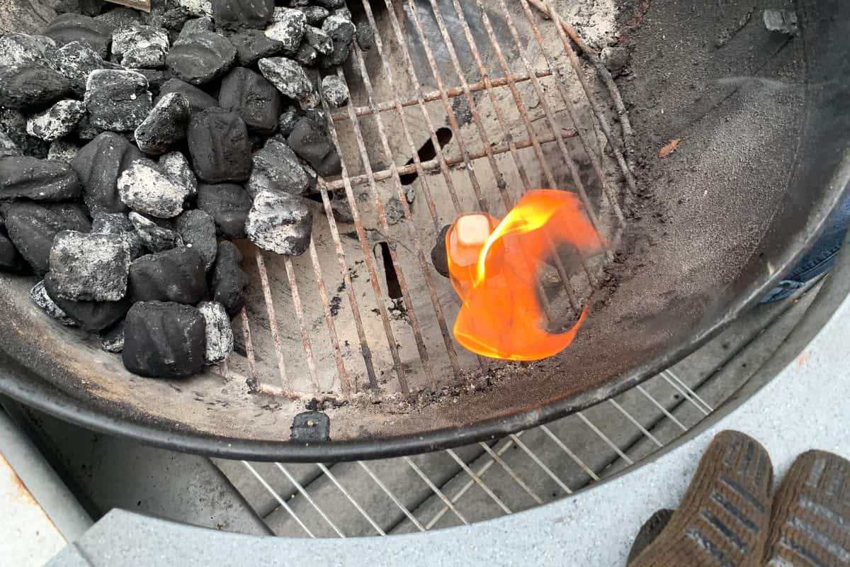 a lit wax lighter cube on top of a charcoal briquette 