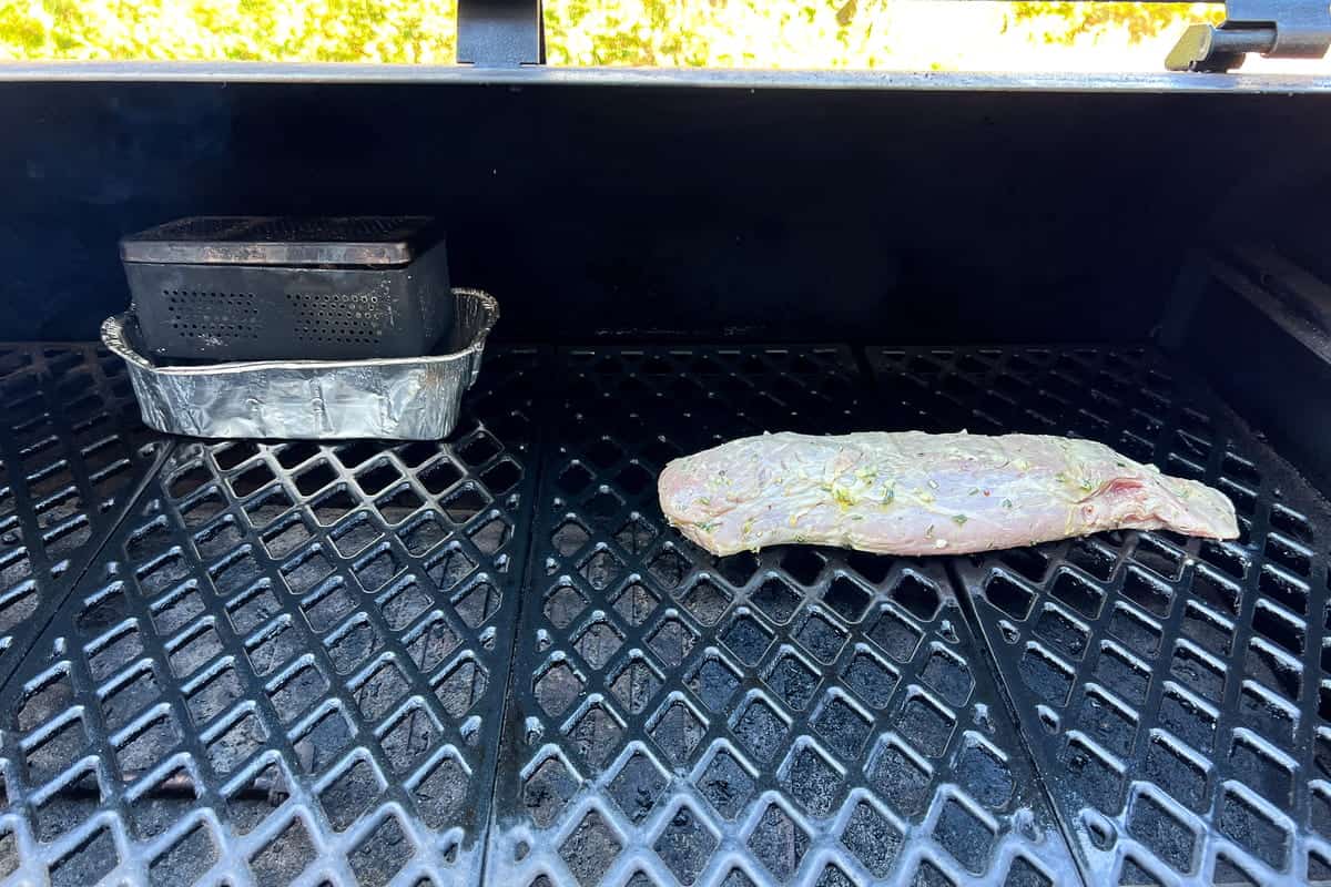 pork tenderloin on the grates of a pit boss with a firebox in the back left of the grill