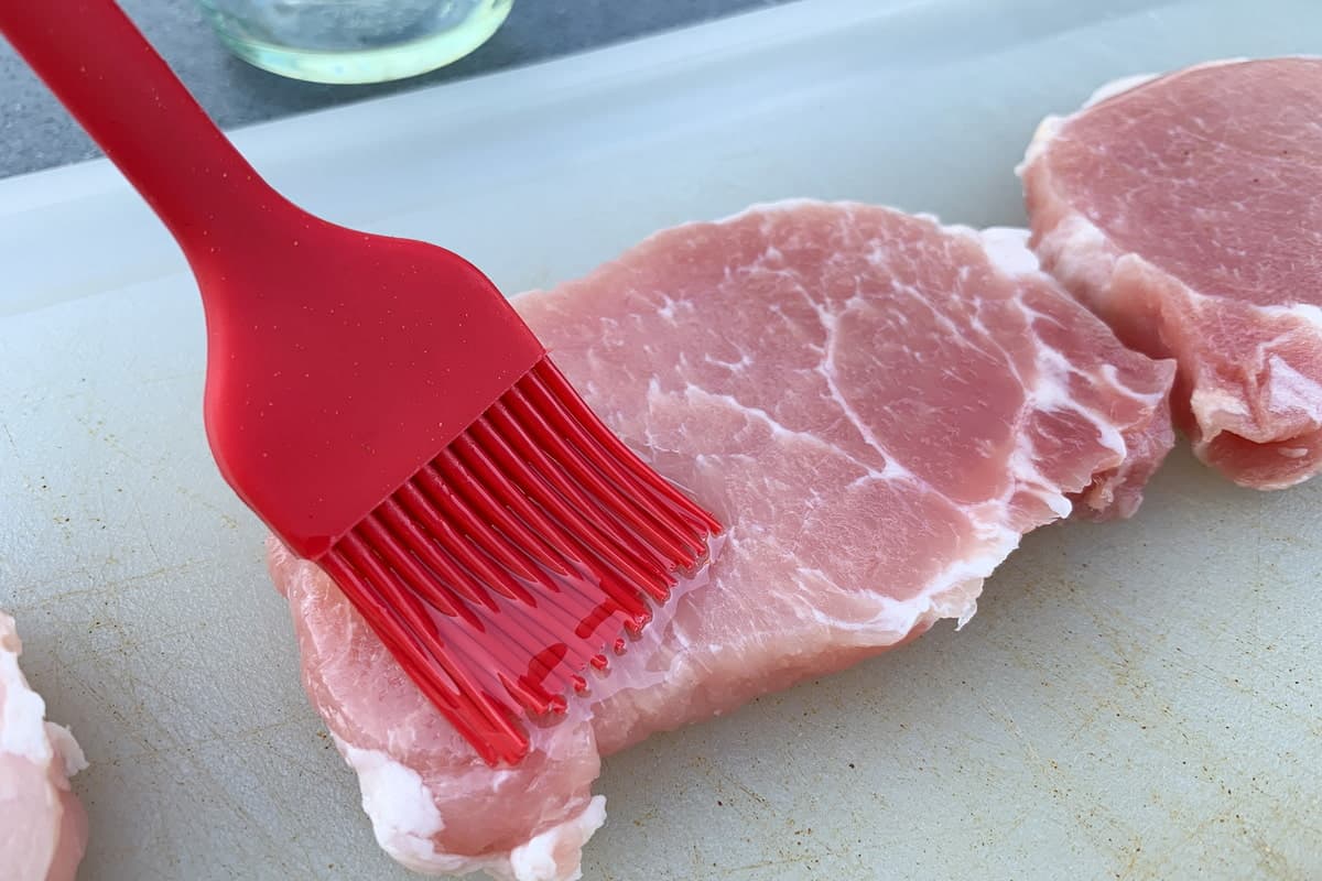 brushing a boneless pork chop with olive oil using a silicone basting brush