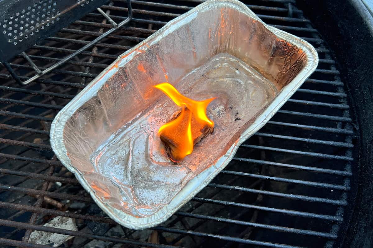 a lit firestarter block burning in an aluminum foil loaf pan