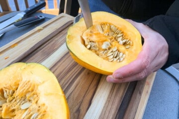 a knife running along the inside of an acorn squash to loosen the seeds and pulp