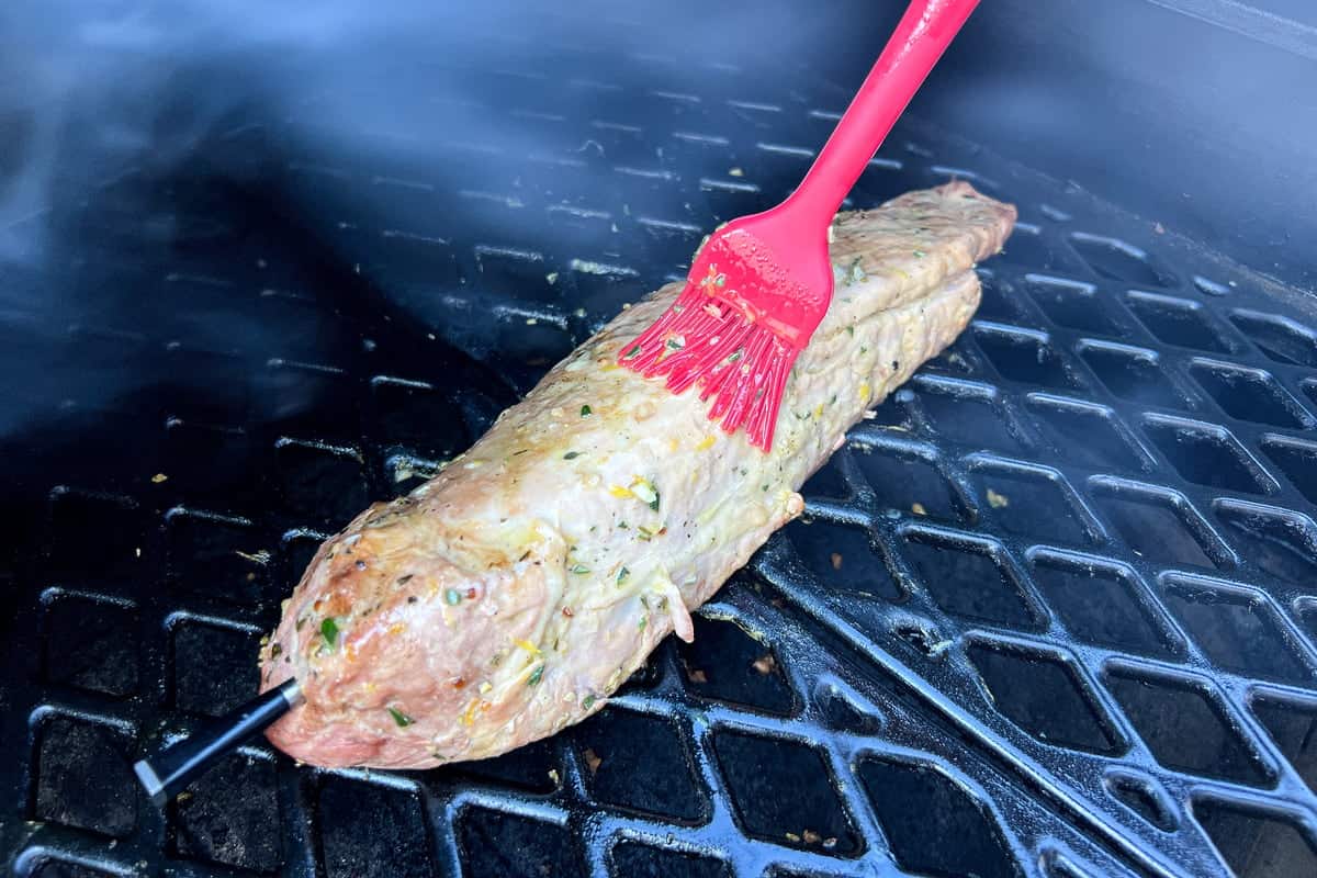 a silicone basting brush brushing garlic herb marinade onto a pork loin on a grill