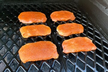 seasoned pork chops evenly spaced on the grates of a pellet grill