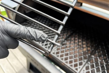 a gloved finger pointing to the grate on the top rack that extends further than the others