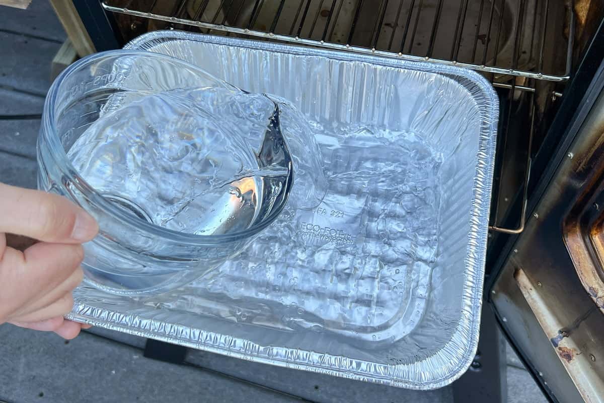 pouring water from a glass measuring cup into an aluminum foil pan