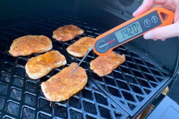 pork chops on the grill grates with an instant read thermometer reading 142 degrees F