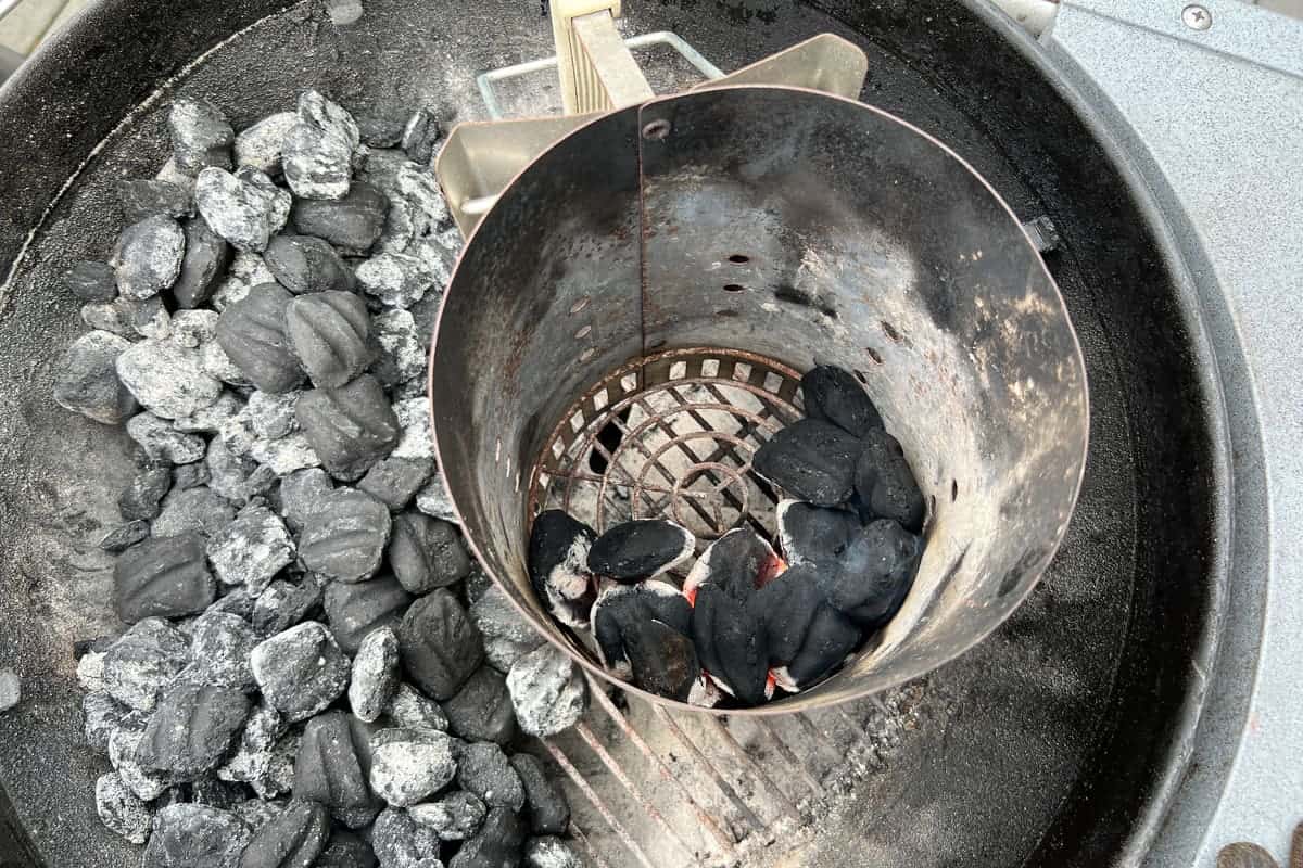 a charcoal chimney partially filled with charcoal briquettes set on top of a lit wax cube