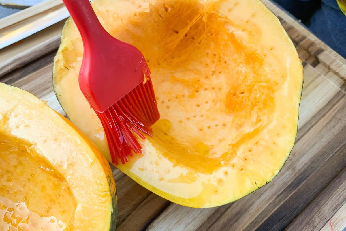 a small silicone spatula brushing olive oil on the side of an acorn squash