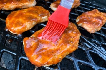 boneless pork chop being brushed with bbq sauce using a silicone basting brush