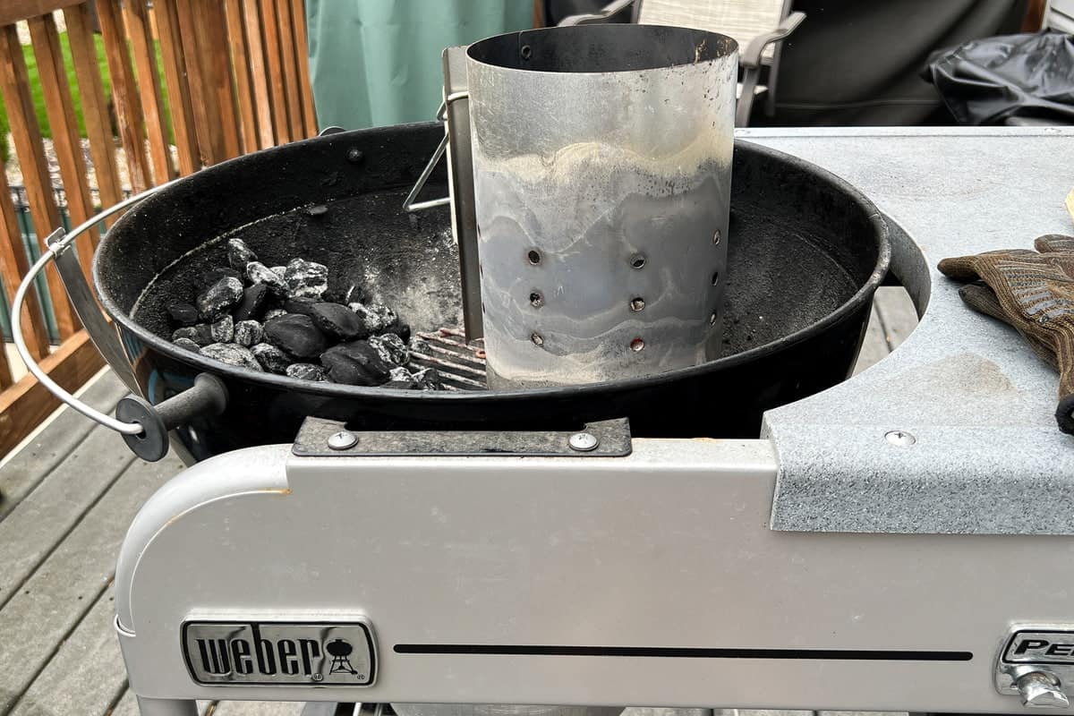 a lit smoking charcoal chimney starter on a charcoal grill