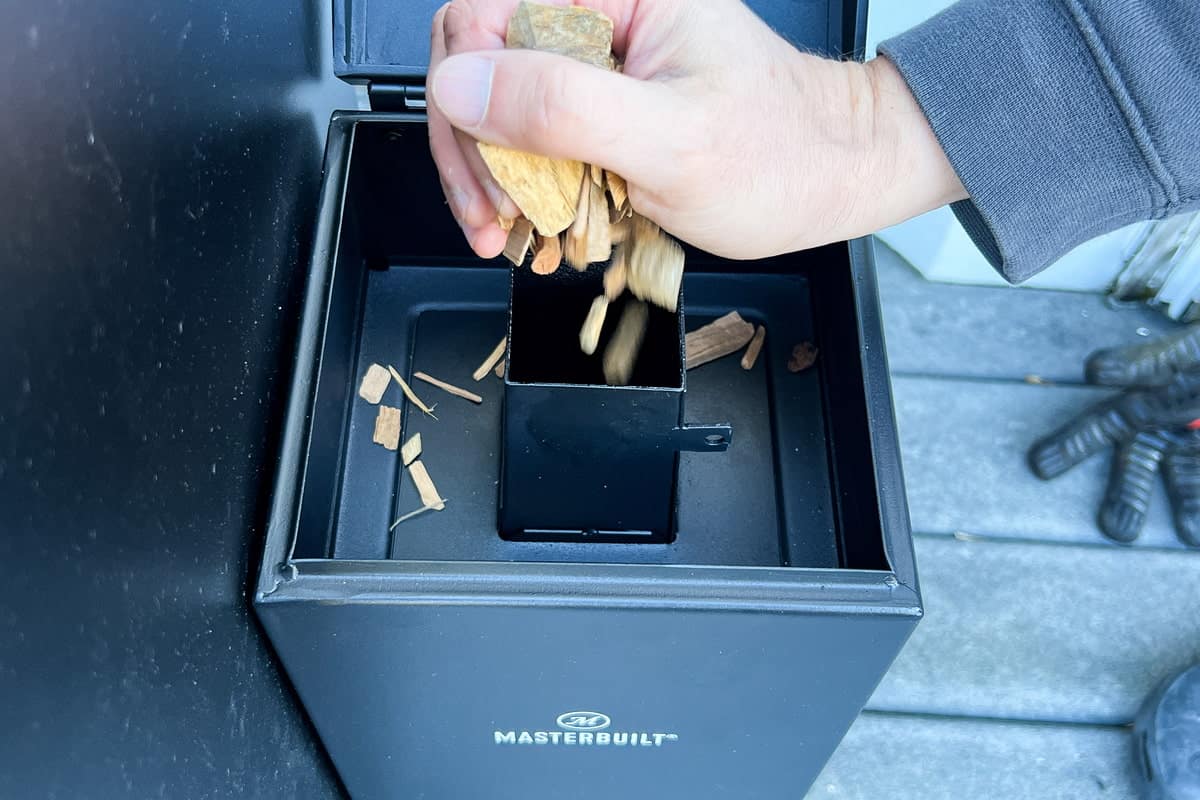 a hand placing wood chips into the Masterbuilt cold smoker attachment