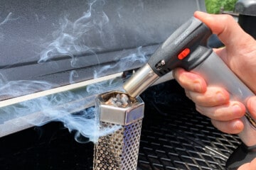 close up of a culinary butane torch igniting pellets in a pellet smoker tube